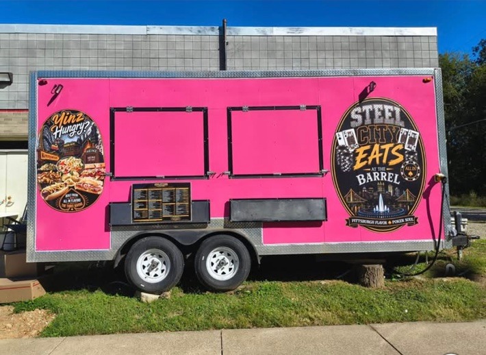Hot pink Steel City Eats food trailer parked beside the Barrel Social Club, with the Steel City Eats at the Barrel emblem and a Yinz Hungry? panel on its side